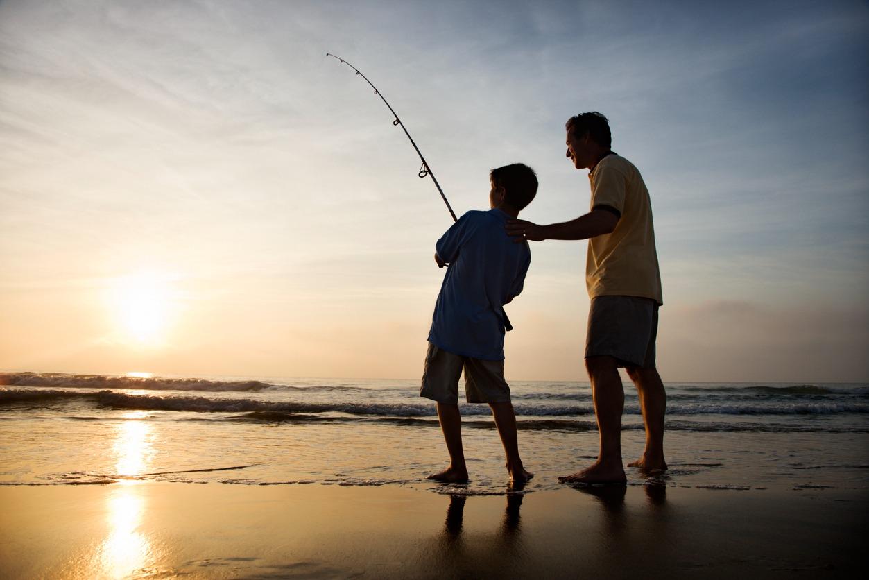 Father and son fishing in ocean surf at sunset. Horizontal shot