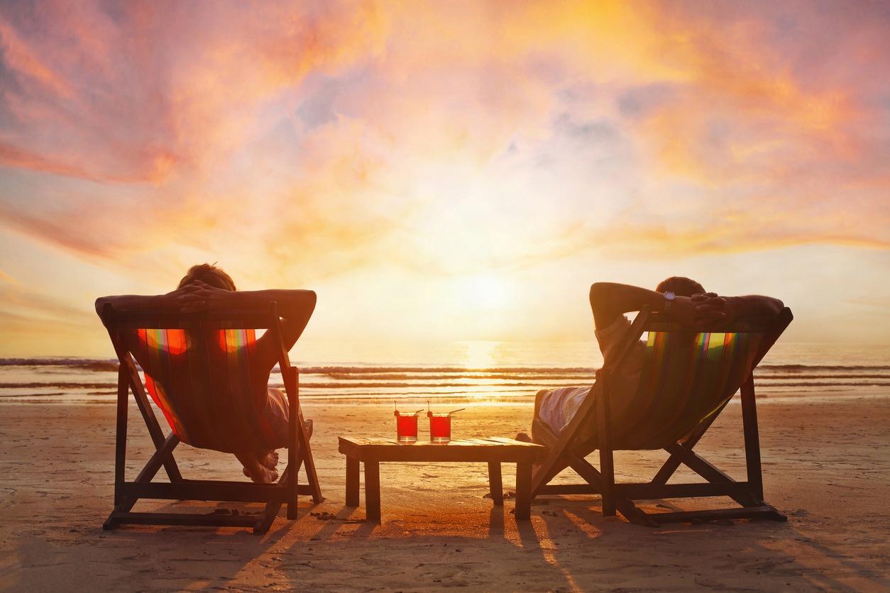 Happy retired couple relaxing on the beach during sunset